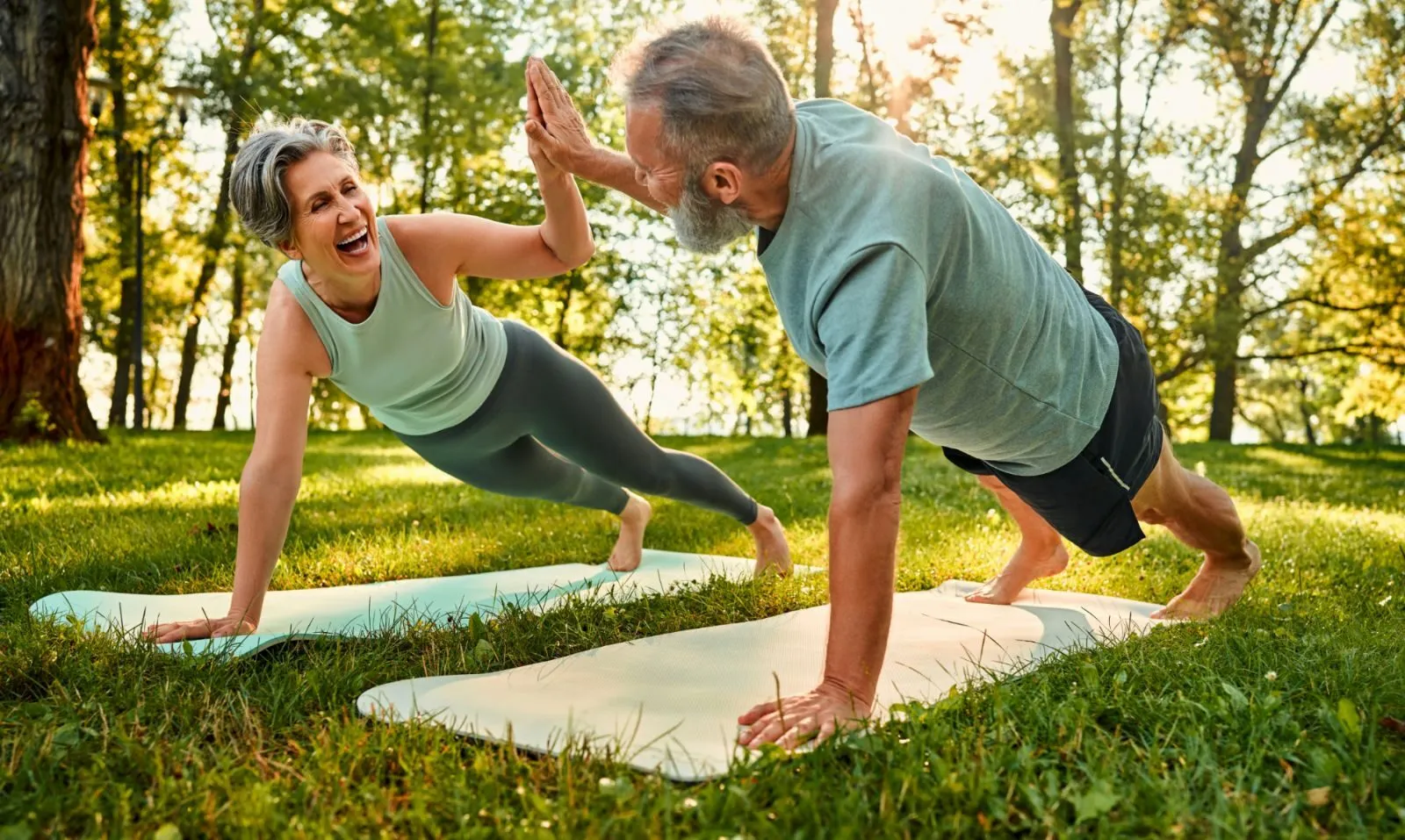 Older couple high-fiving while exercising on yoga mats outdoors